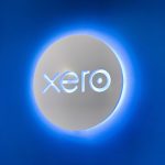 Illuminated, back-lit white sign on blue lobby wall for Xero, a cloud-based accounting software platform for small and medium-sized businesses.