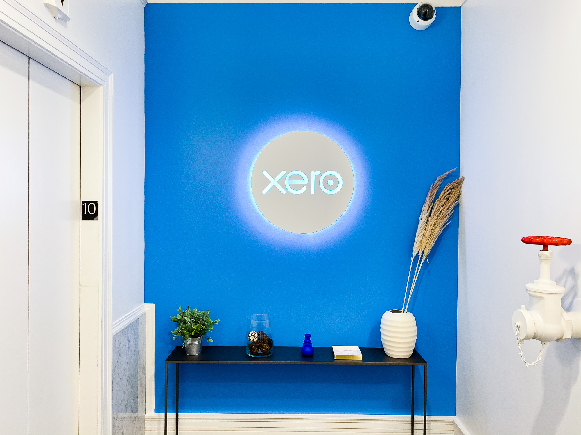 Illuminated, back-lit white sign on blue lobby wall for Xero, a cloud-based accounting software platform for small and medium-sized businesses.