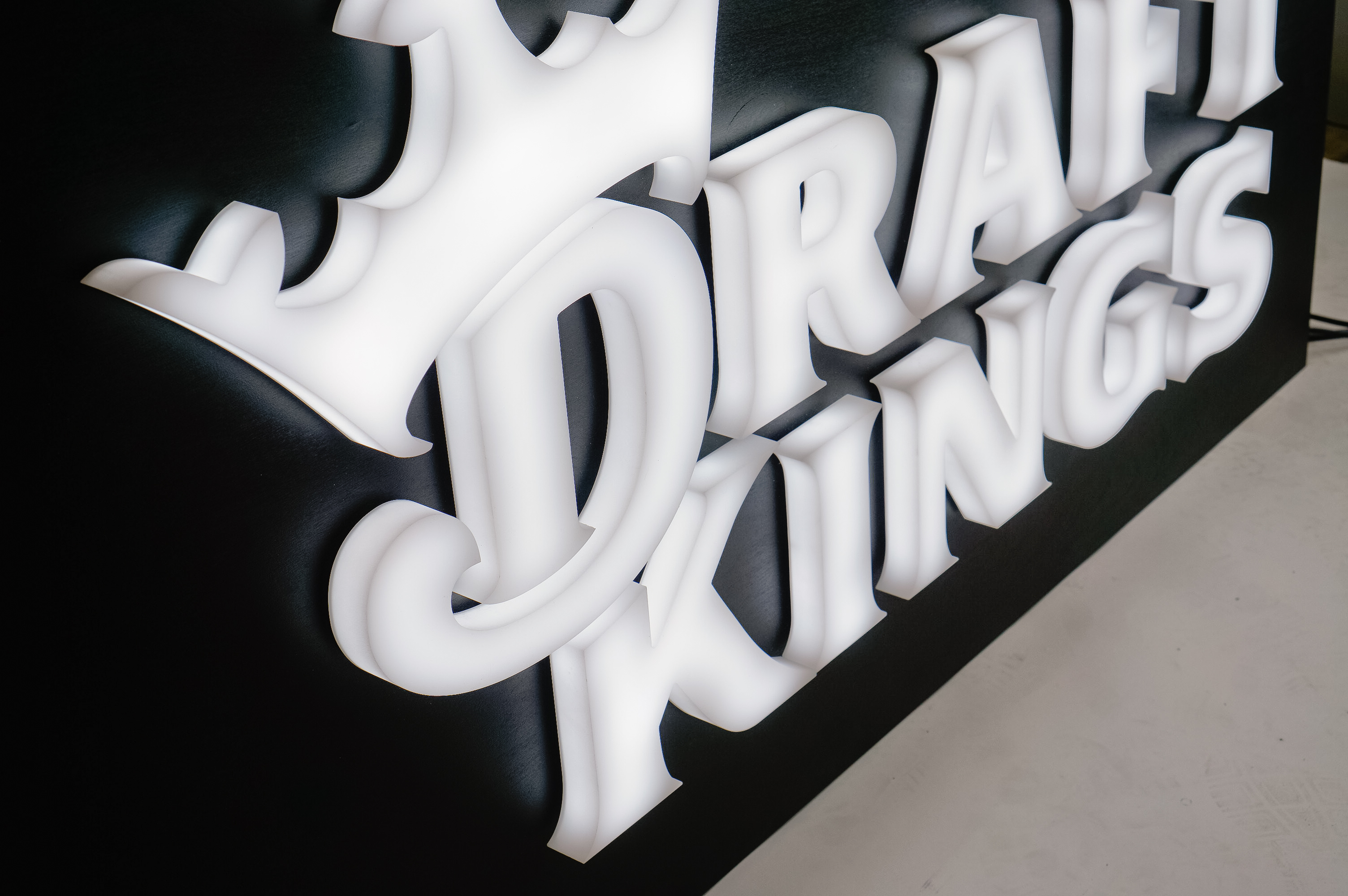 Illuminated, face-lit white logo on a black painted backer/wall for the San Francisco office of Draft Kings, an American daily fantasy sports contest and sports betting provider.