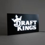 Illuminated, face-lit white logo on a black painted backer/wall for the San Francisco office of Draft Kings, an American daily fantasy sports contest and sports betting provider.