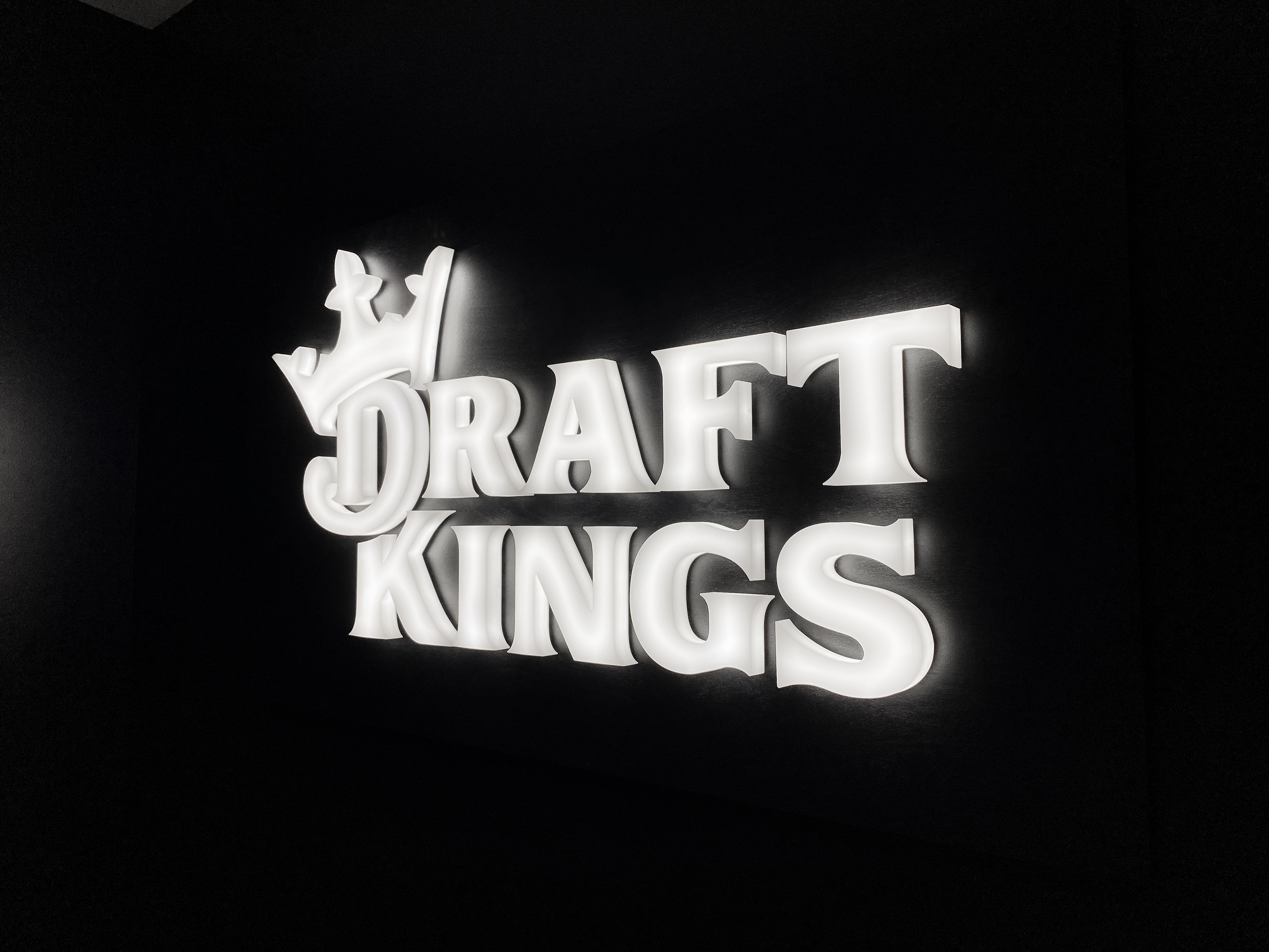Illuminated, face-lit white logo on a black painted backer/wall for the San Francisco office of Draft Kings, an American daily fantasy sports contest and sports betting provider.