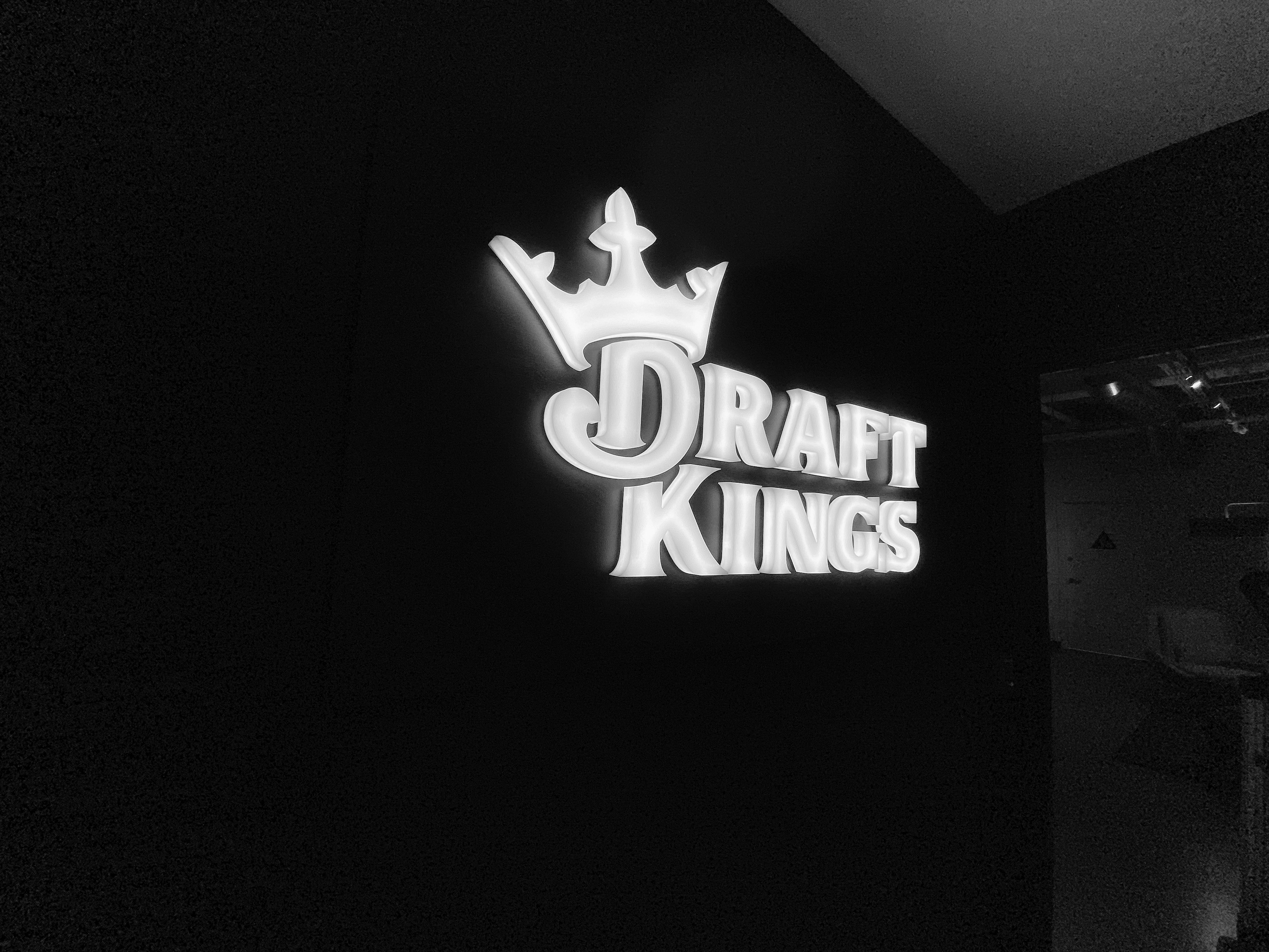 draft-kings-site2 Illuminated, face-lit white logo on a black painted backer/wall for the San Francisco office of Draft Kings, an American daily fantasy sports contest and sports betting provider.