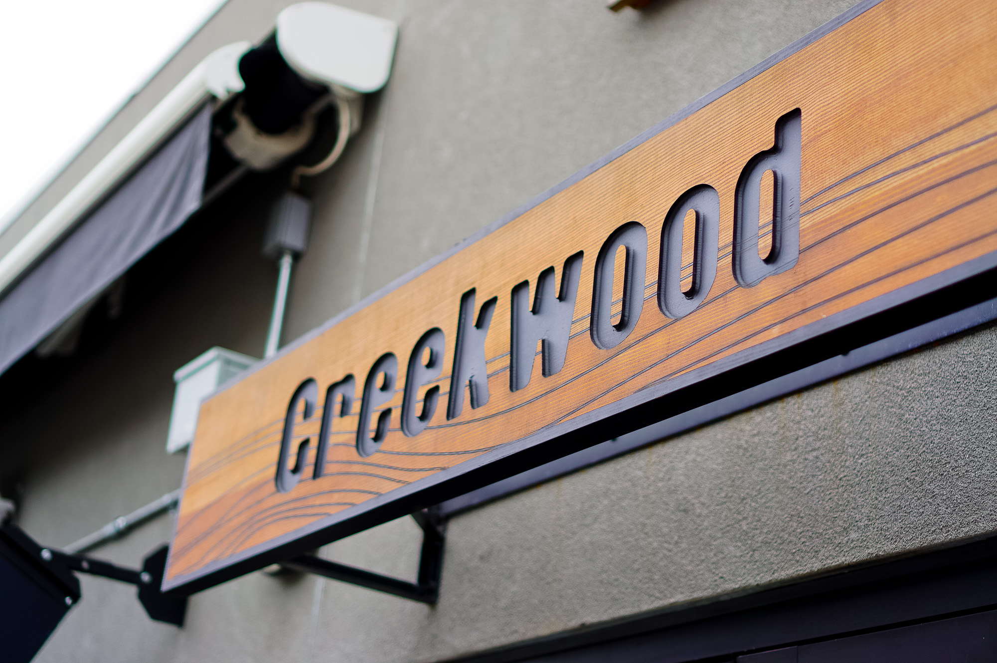 Engraved cedar wood sign on concrete walkl for Creekwood, a Californian-Italian restaurant in Berkeley, CA