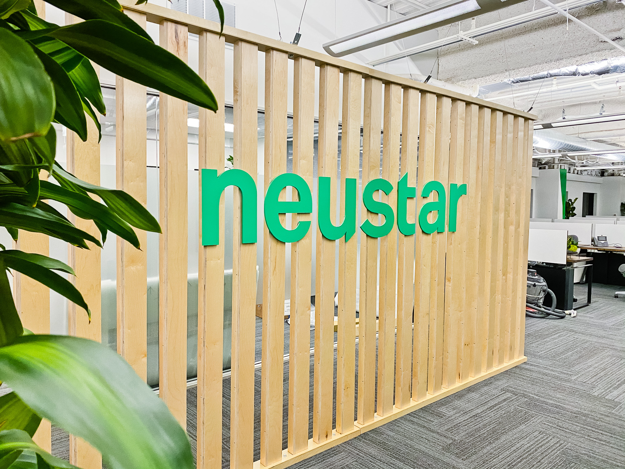 Wood slat dividing wall wiht green logo for lobby/reception desk area at the San Francisco office of Neustar, an American technology company that provides real-time information and analytics.