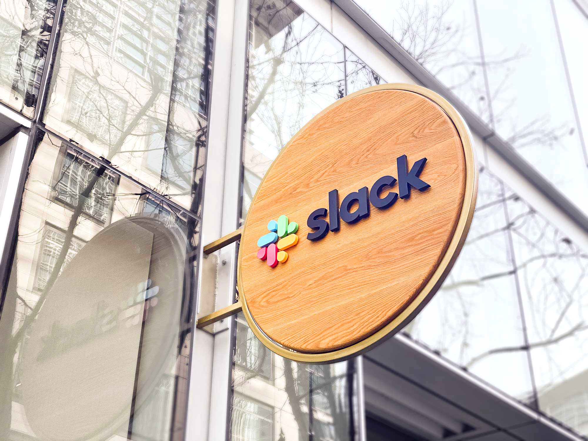 Wood blade sign with dimensional color logo and brass hardware for the San Francisco brand space at Slack, an American cloud-based set of team collaboration tools and services.
