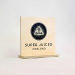Light wood tabletop sign with black print for the retail location of Super Juiced, an organic juice and smoothie bar in Old Oakland.