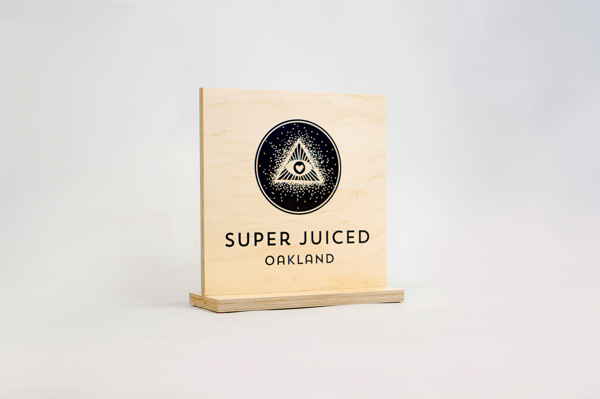 Light wood tabletop sign with black print for the retail location of Super Juiced, an organic juice and smoothie bar in Old Oakland.