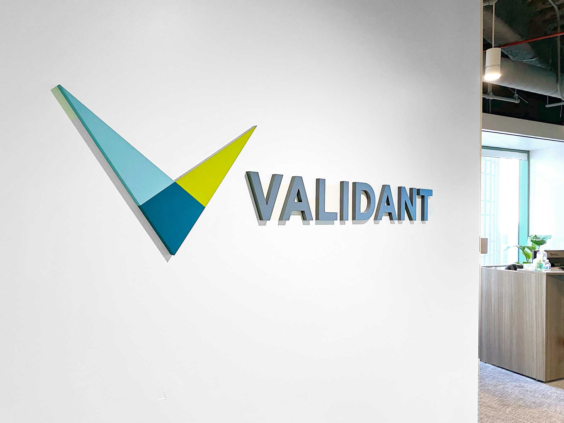 Full color dimensional logo on white wall for the lobby of Validant, a San Francisco based company that delivers end-to-end quality, compliance, and regulatory consulting service for healthcare companies around the world.