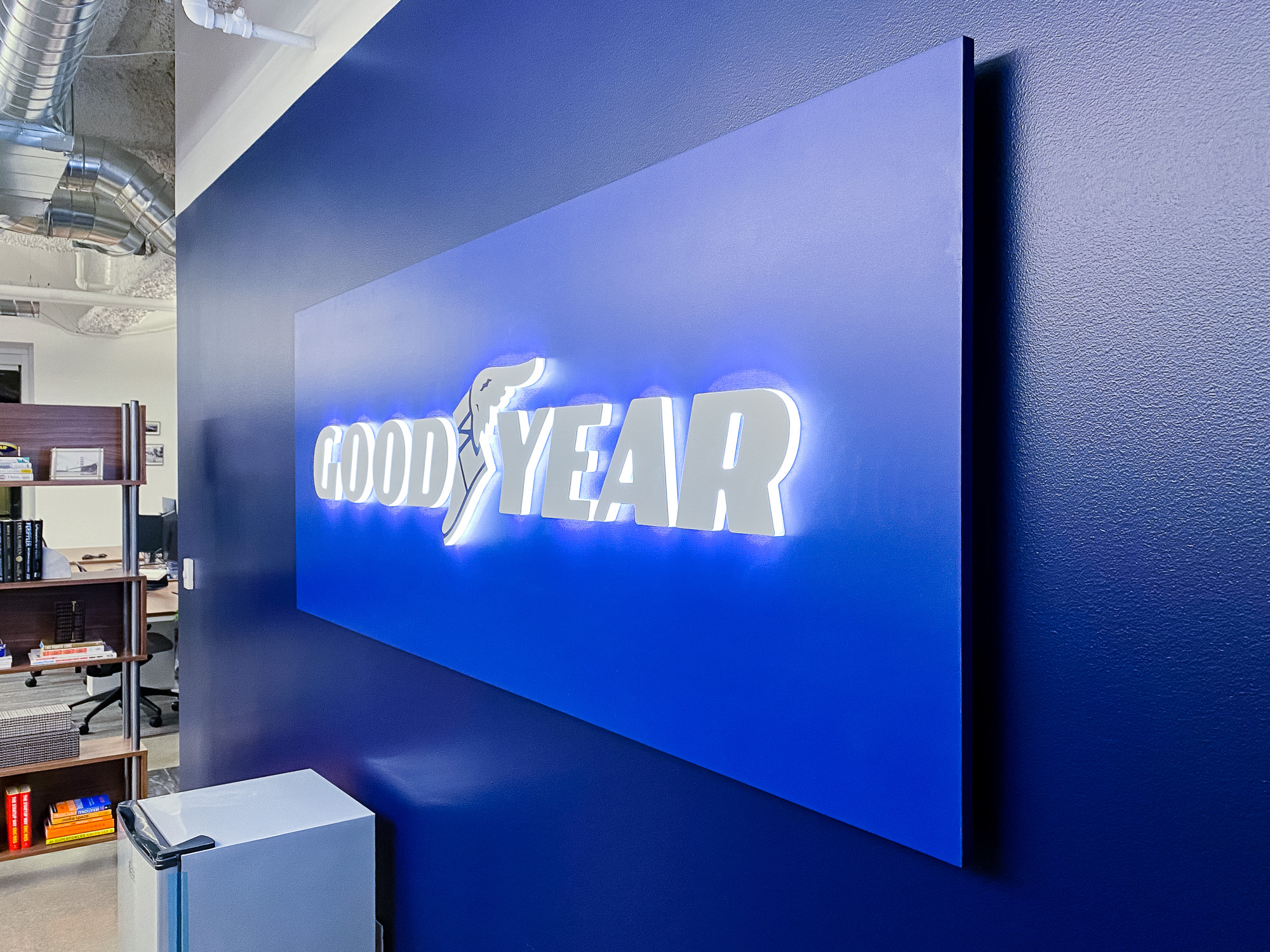 Illuminated, blue, edge-lit lobby sign behind reception desk for the San Francisco office of Goodyear, a tire manufacturer.