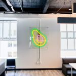 Neon avocado sign with clear acrylic backer on white wall for the San Francisco office of Meltwater, a software as a service company that develops and markets media monitoring and business intelligence software.