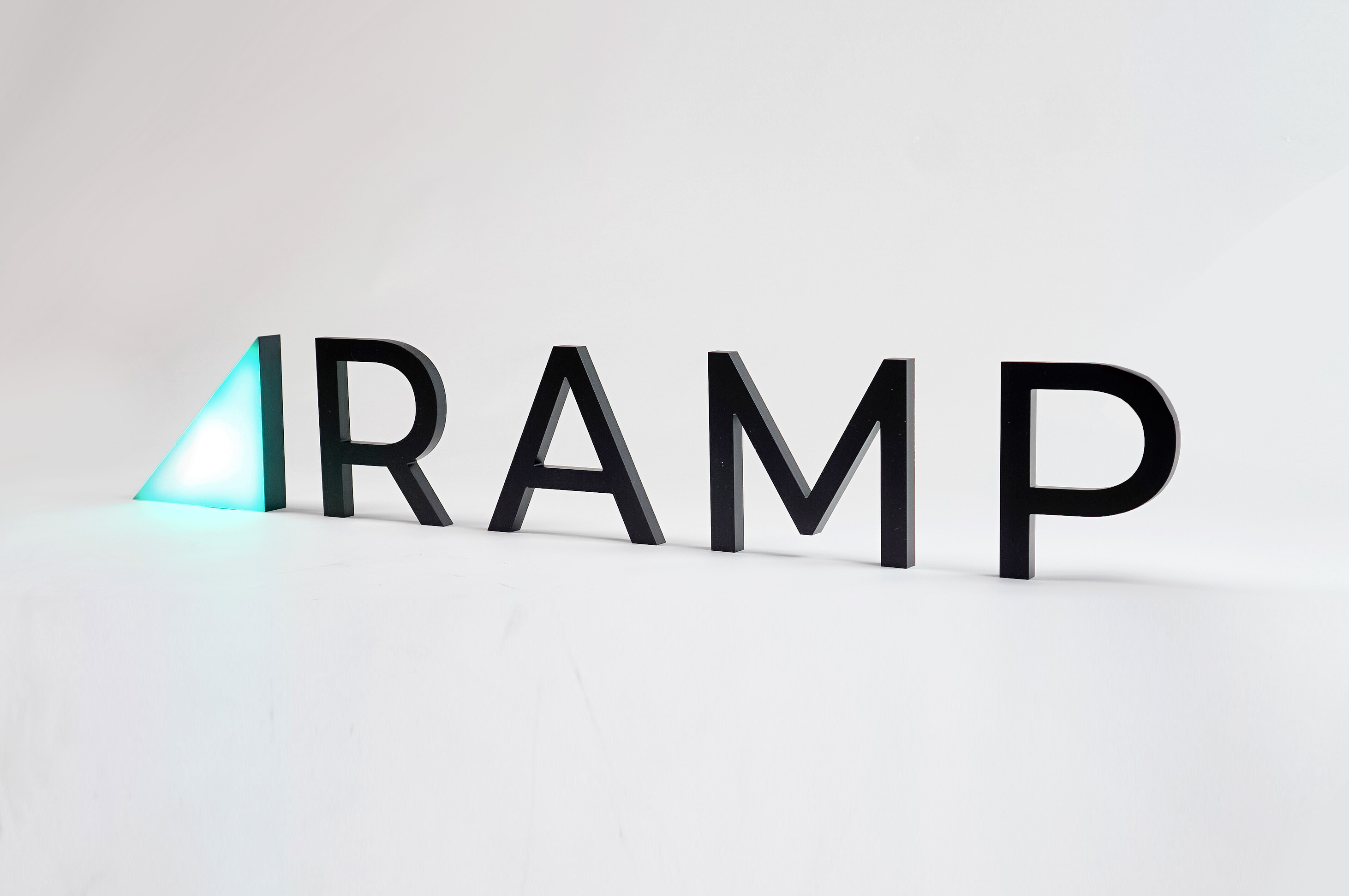 Illuminated, freestanding green triangle and black letters for Ramp, a technology company building the next generation corporate card to save businesses money.