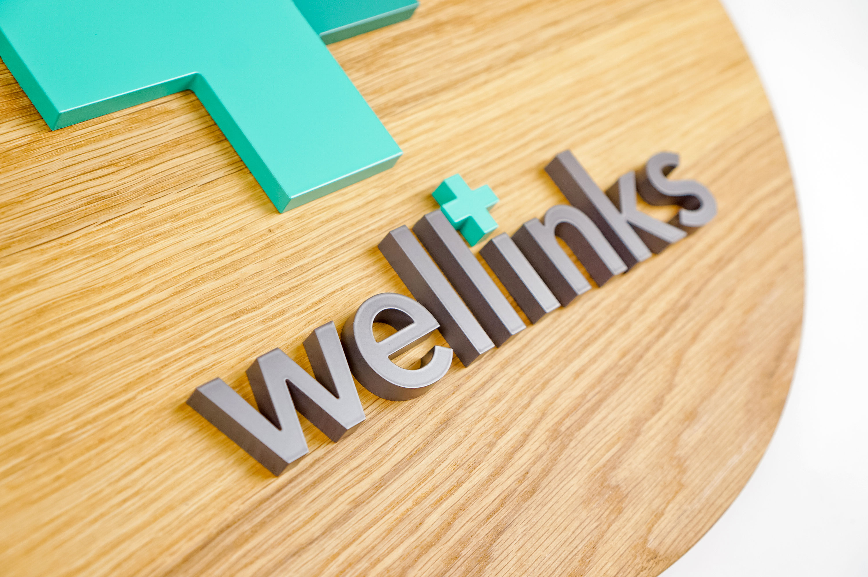Wood hanging blade sign with green and grey logo for Wellinks, a wearable health technology company.