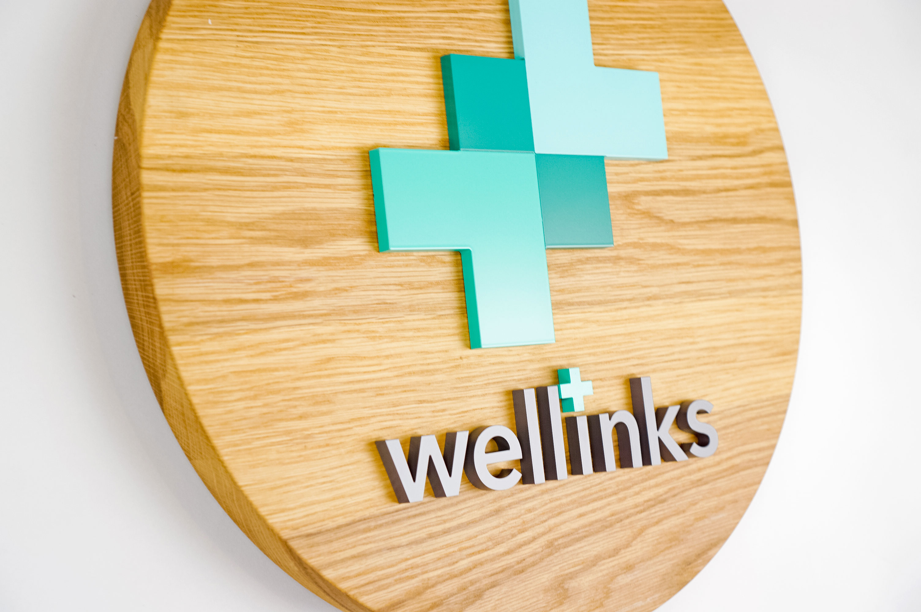 Wood hanging blade sign with green and grey logo for Wellinks, a wearable health technology company.