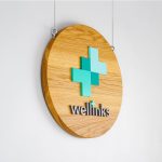 Wood hanging blade sign with green and grey logo for Wellinks, a wearable health technology company.