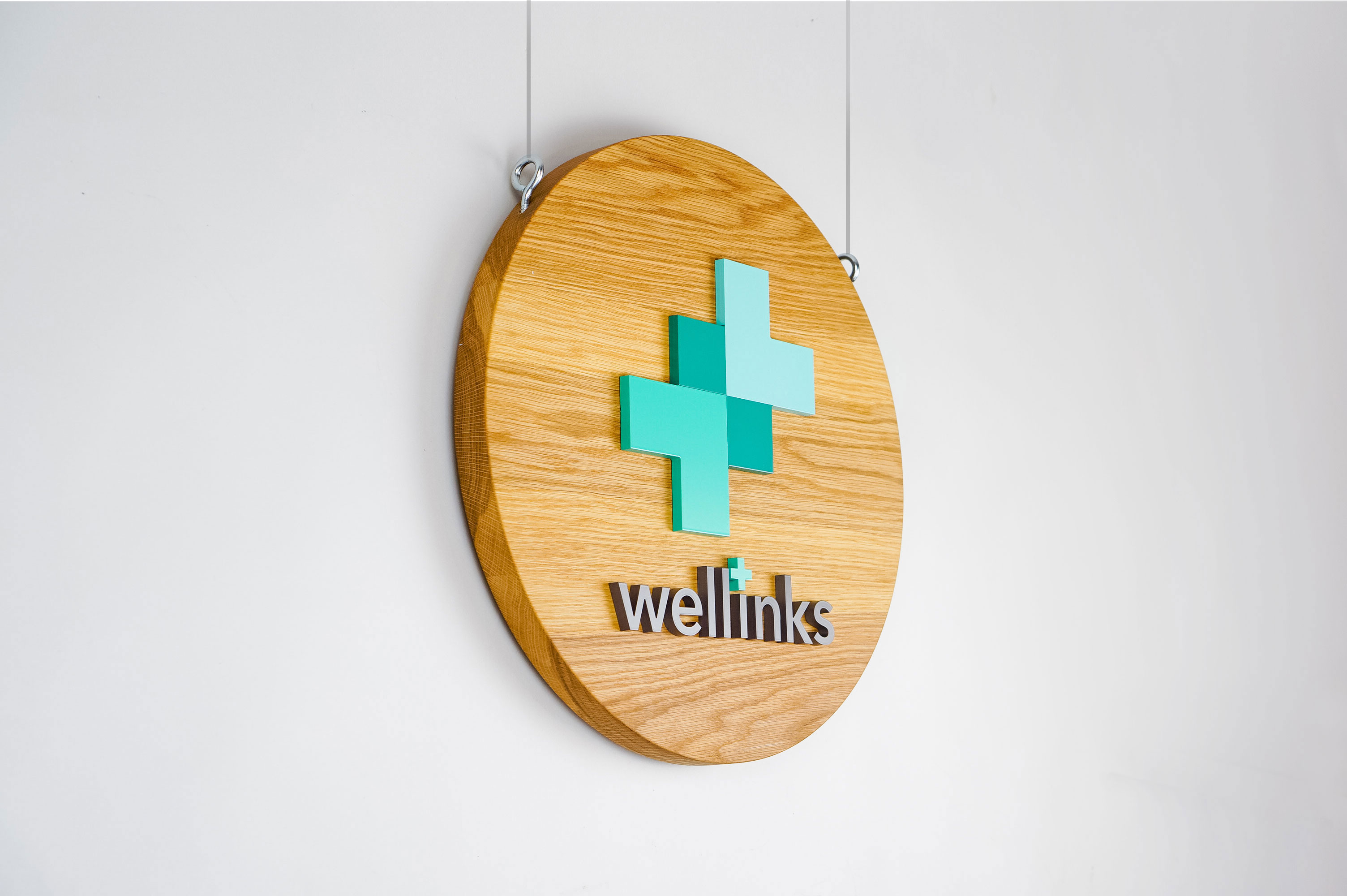 Wood hanging blade sign with green and grey logo for Wellinks, a wearable health technology company. Wood hanging blade sign with green and grey logo for Wellinks, a wearable health technology company.