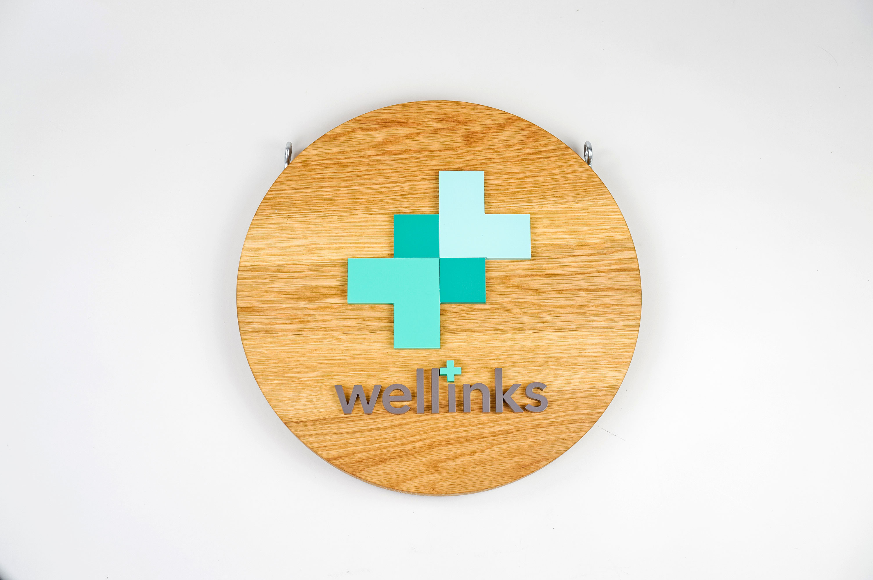 Wood hanging blade sign with green and grey logo for Wellinks, a wearable health technology company.
