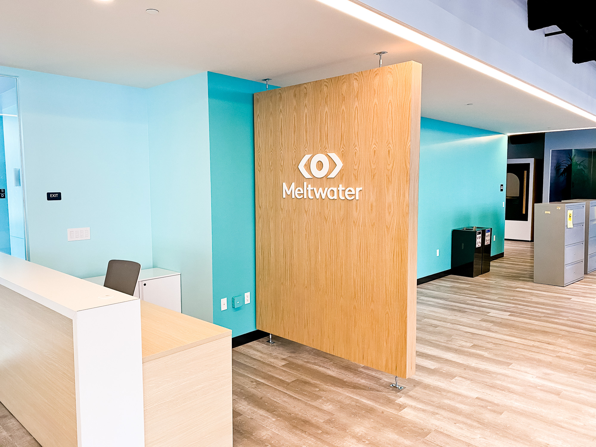 White logo on light wood add-on divider wall for the San Francisco office of Meltwater, a software as a service company that develops and markets media monitoring and business intelligence software.