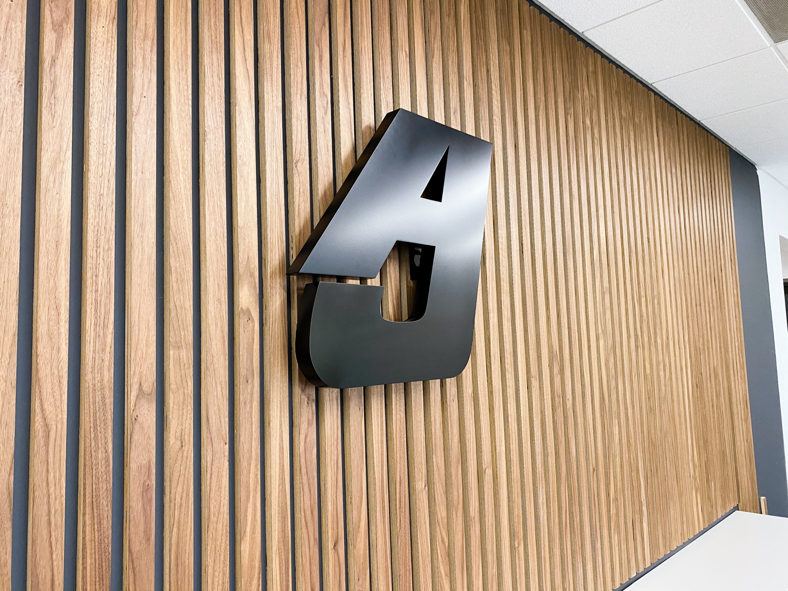 Illuminated, back-lit black sign for slat wood wall for the lobby of Anning-Johnson Company, one of the country’s largest specialty construction companies.