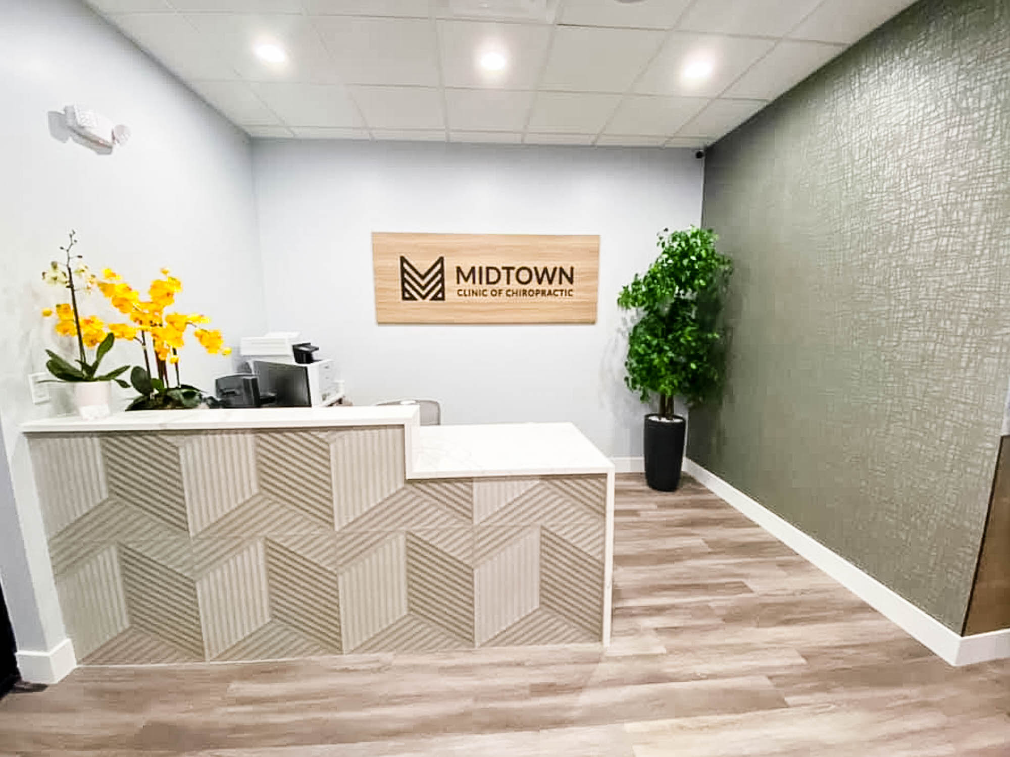 Midtown Clinic of Chiropractic Black logo on light wood laminate panel in the main lobby of the Midtown Clinic of Chiropractic, a full-service chiropractic treatment center serving the Lake Worth, FL area.