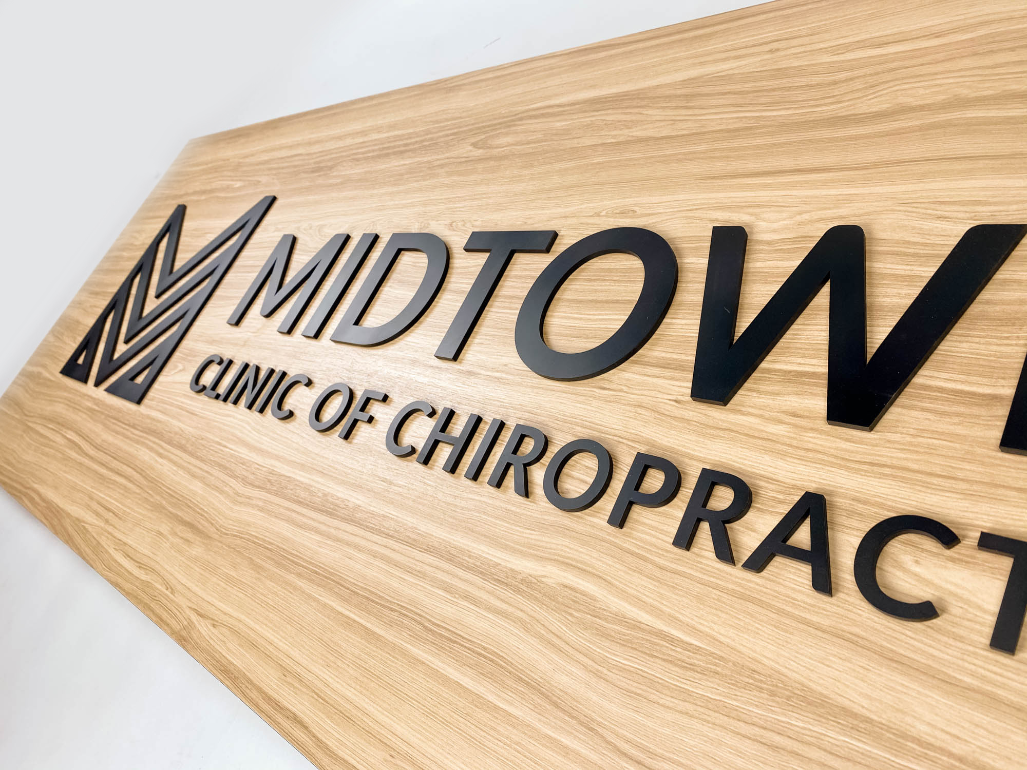Black logo on light wood laminate panel for the Midtown Clinic of Chiropractic, a full-service chiropractic treatment center serving the Lake Worth, FL area.