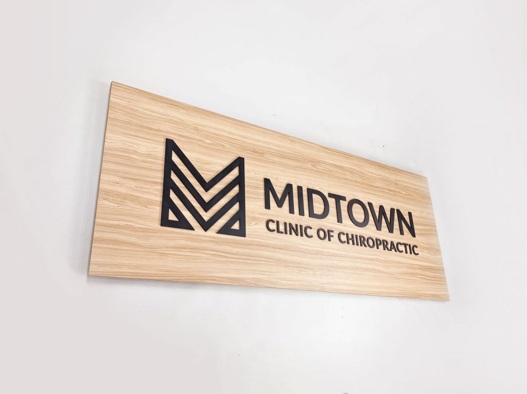 Black logo on light wood laminate panel for the Midtown Clinic of Chiropractic, a full-service chiropractic treatment center serving the Lake Worth, FL area.