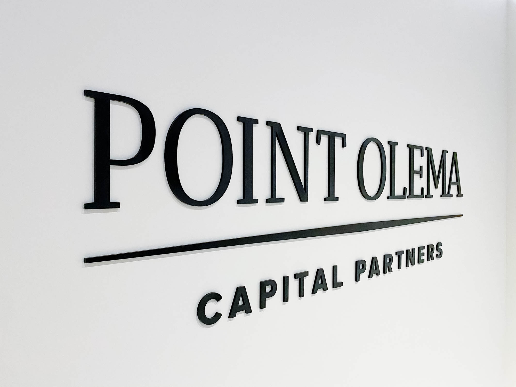 Point Olema Simple black lobby sign on painted wall with uplights for the San Francisco office of Point Olema Capital Partners.