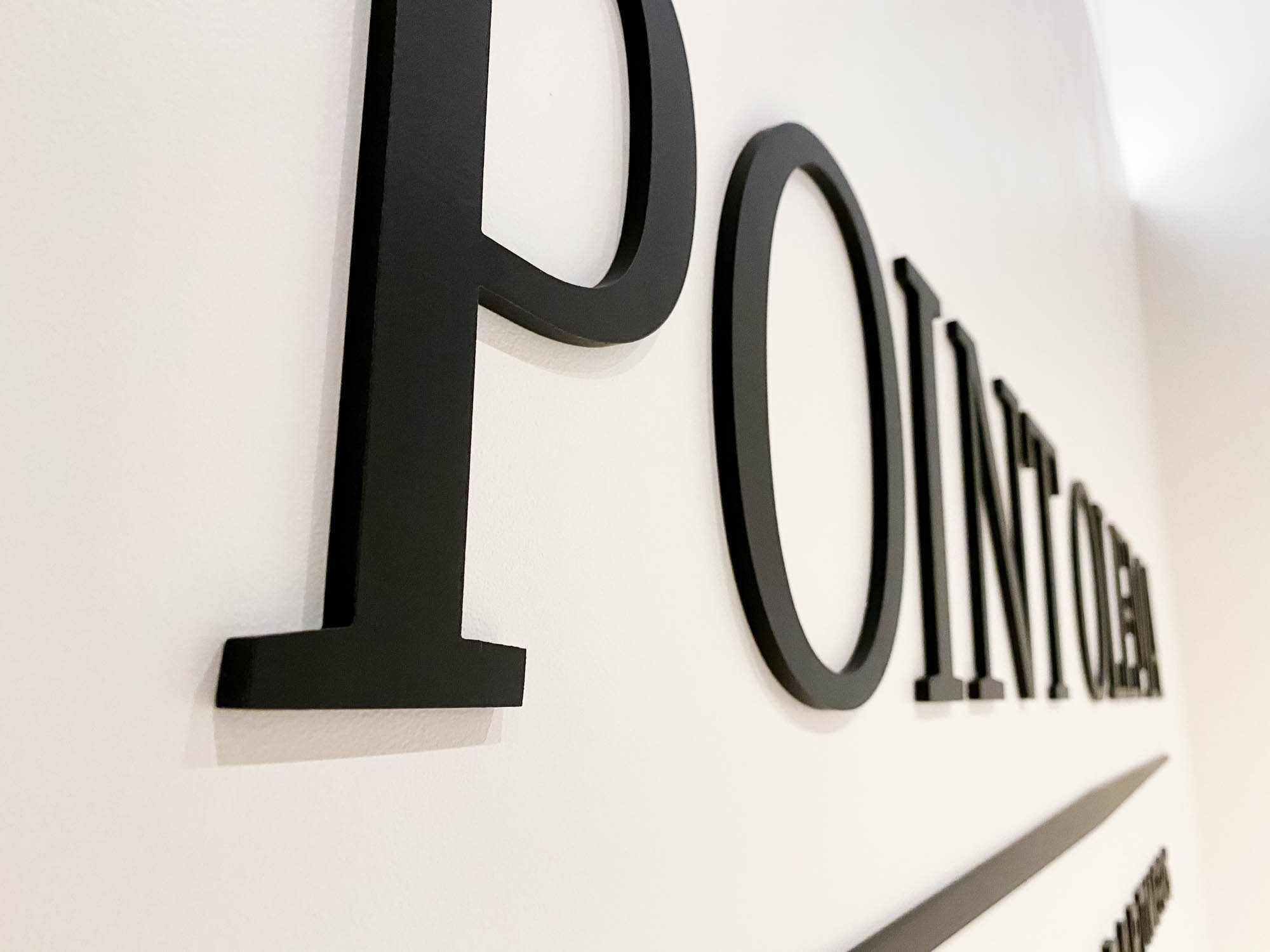 Point Olema Simple black lobby sign on painted wall with uplights for the San Francisco office of Point Olema Capital Partners.