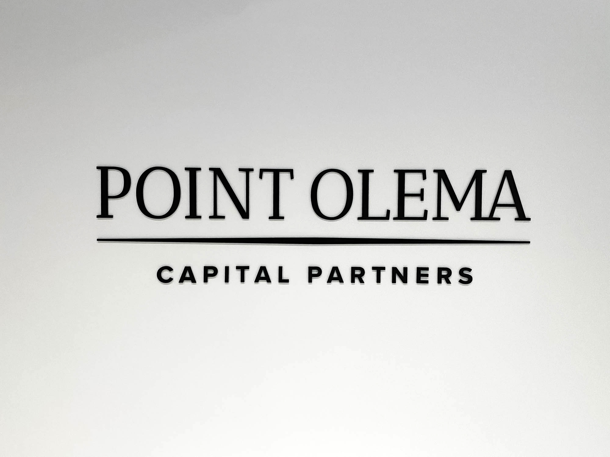 Simple black lobby sign on painted wall with uplights for the San Francisco office of Point Olema Capital Partners.