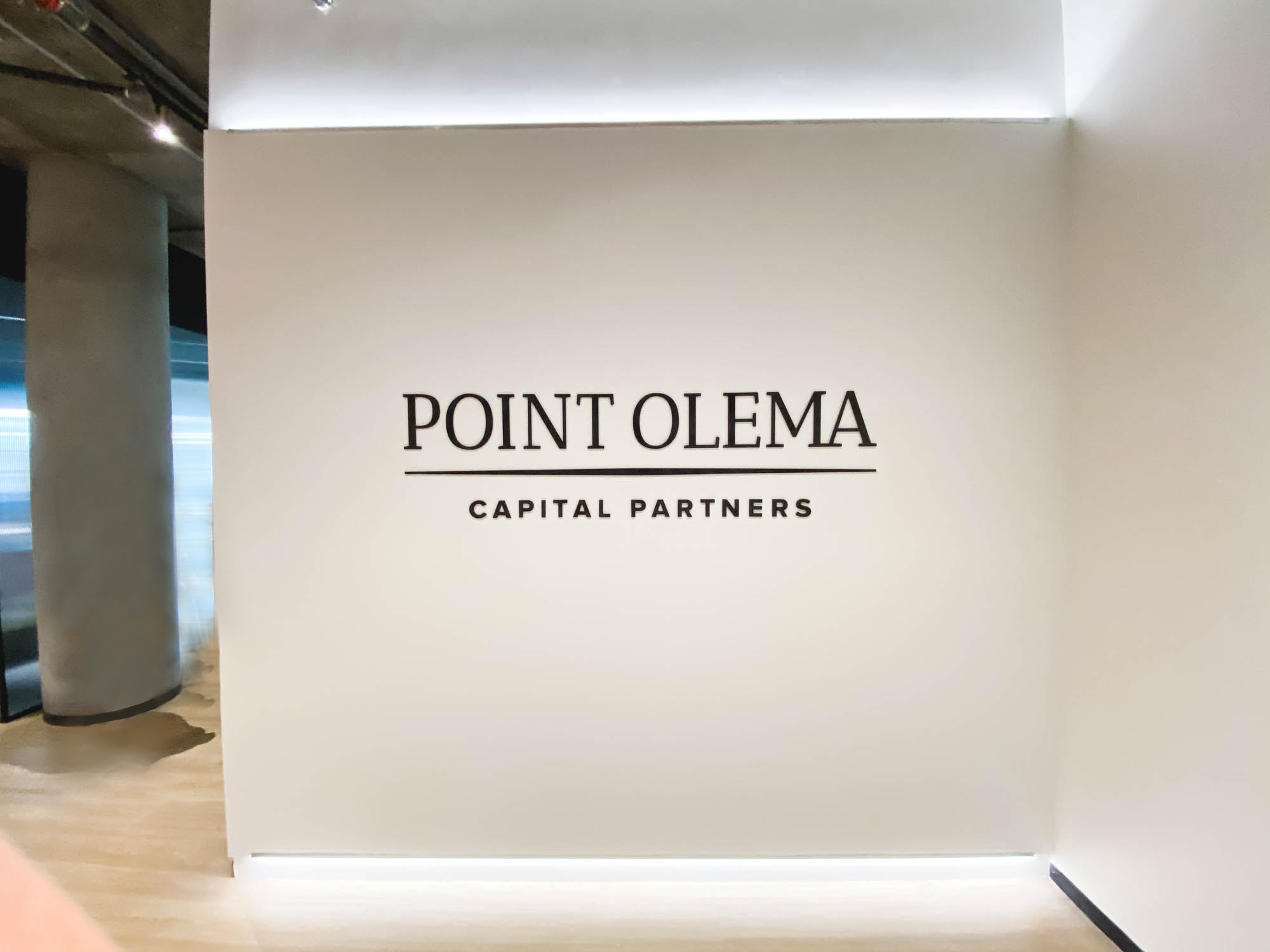 Simple black lobby sign on painted wall with uplights for the San Francisco office of Point Olema Capital Partners.