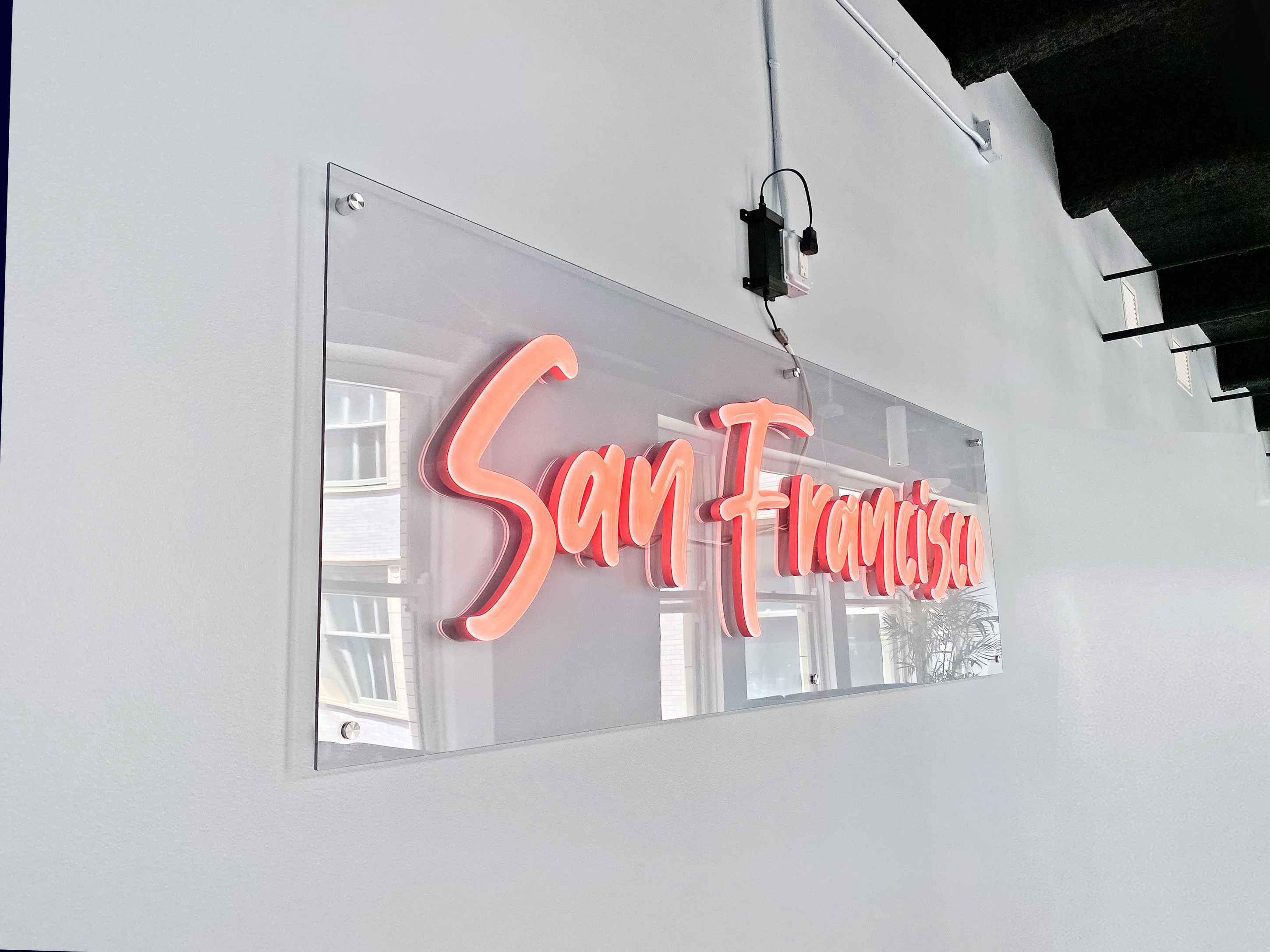 Pink script LED neon sign on clear backer for the San Francisco office of Meltwater, a software as a service company that develops and markets media monitoring and business intelligence software.