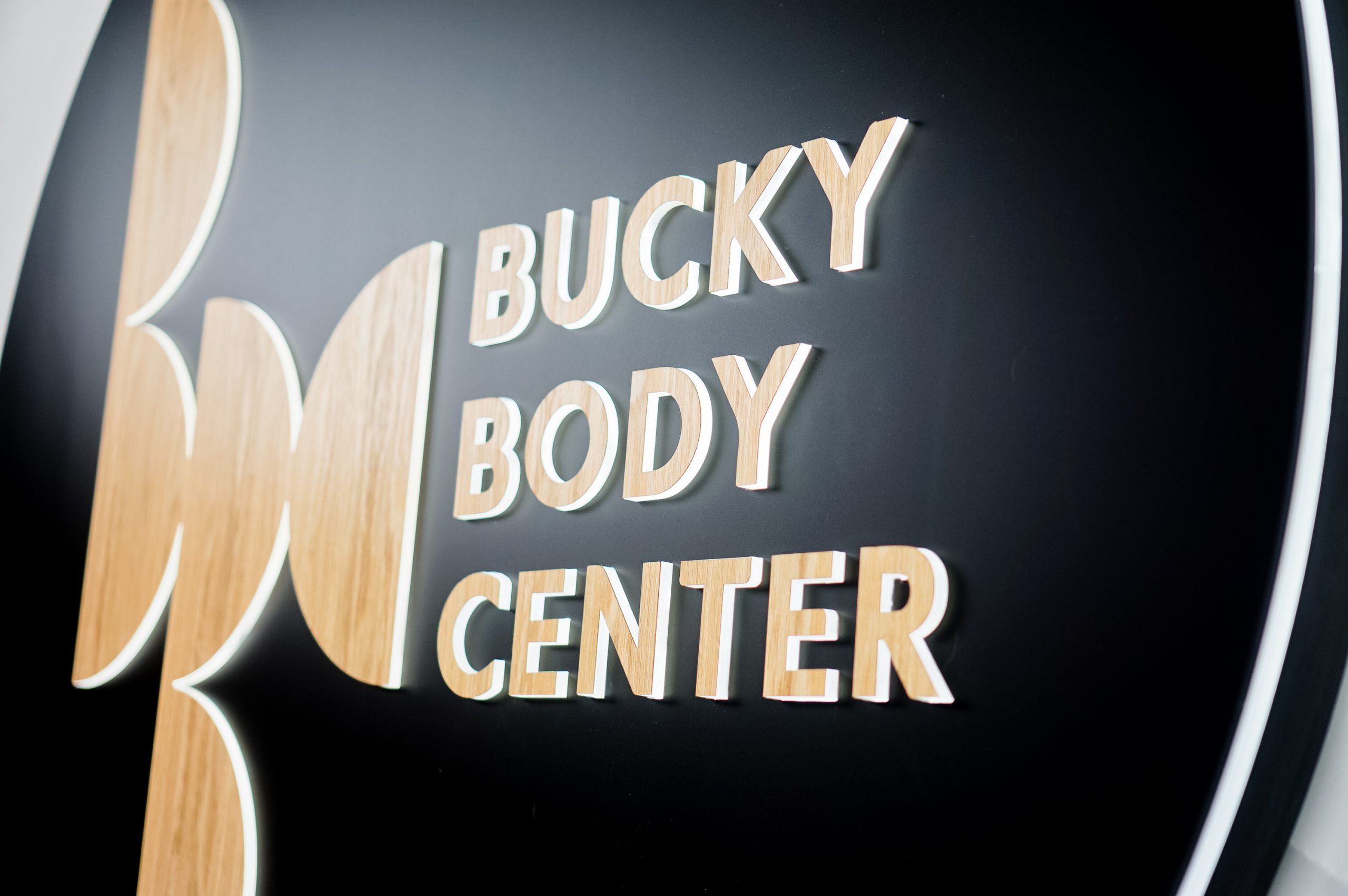 Illuminated, black and light wood edge-lit sign on moss wall for the Bucky Body Center, a body plastic and reconstructive surgery center in Philadelphia, PA.