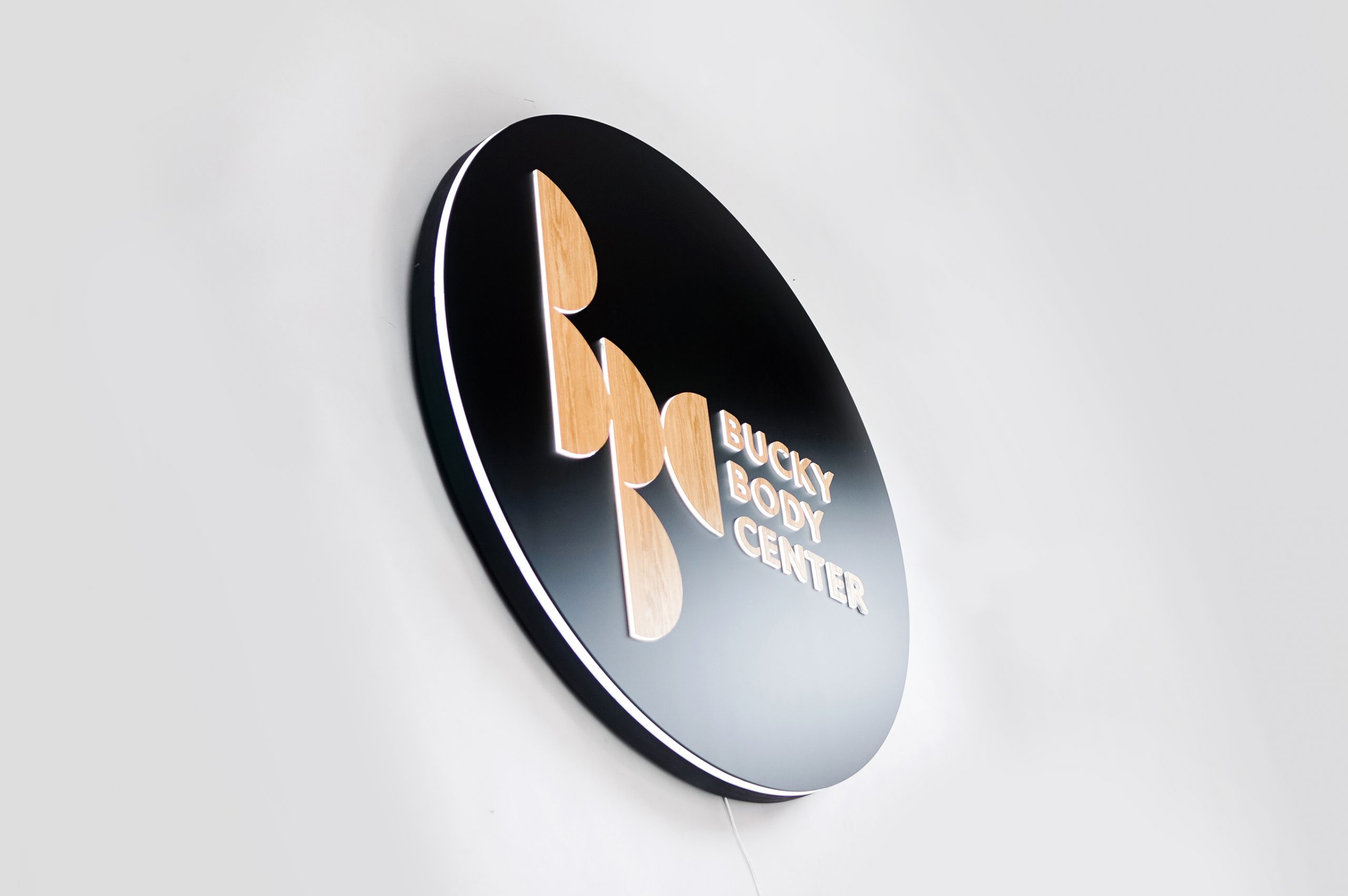 Illuminated, black and light wood edge-lit sign on moss wall for the Bucky Body Center, a body plastic and reconstructive surgery center in Philadelphia, PA.