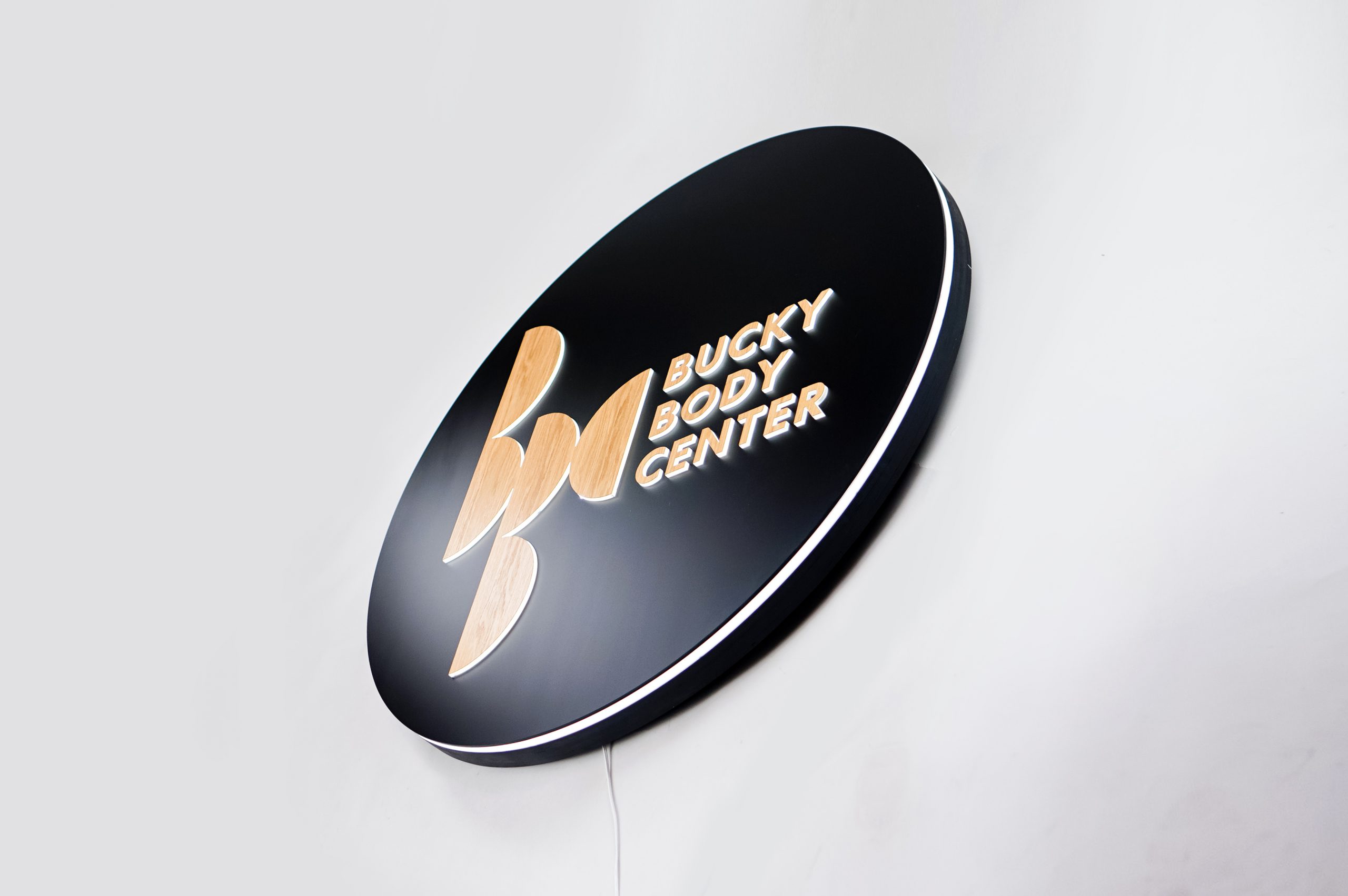 Illuminated, black and light wood edge-lit sign on moss wall for the Bucky Body Center, a body plastic and reconstructive surgery center in Philadelphia, PA.