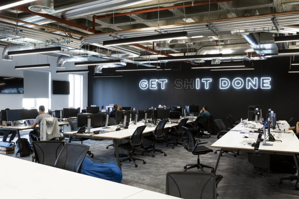 White neon "Get Shit Done" sign on black painted wall in the main office space of Revolut in London, England. (Photo: Tom Fallon)