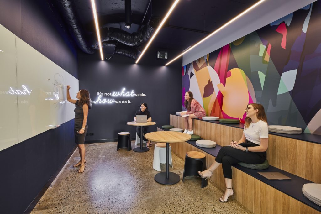 Neon motto on black wall in tiered seating office room at Over the Wire in Brisbane, Australia. (Photo: Cieran Murphy Photography)