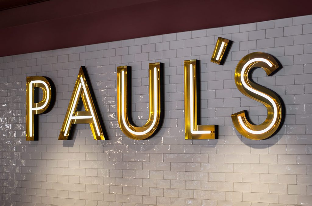 Neon sign in gold open face channel letters on white tile wall for Paul, a restaurant in Stockholm, Sweden. (Photo: 25AH)