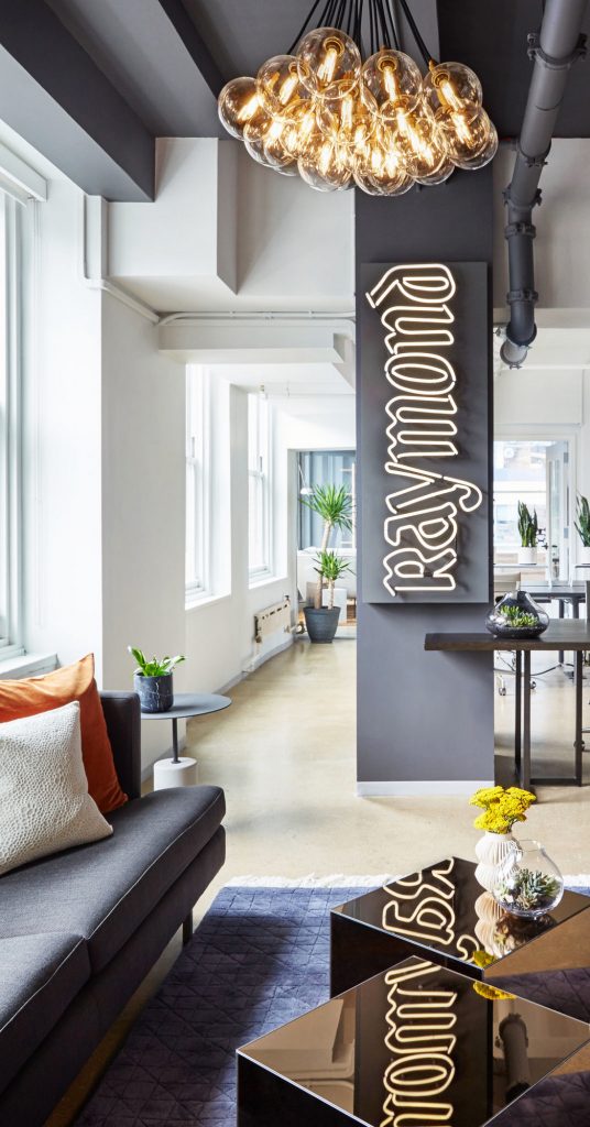 White neon sign with clear backer on grey painted wall for the office of Raymond in New York. (Photo: Seth Caplan)