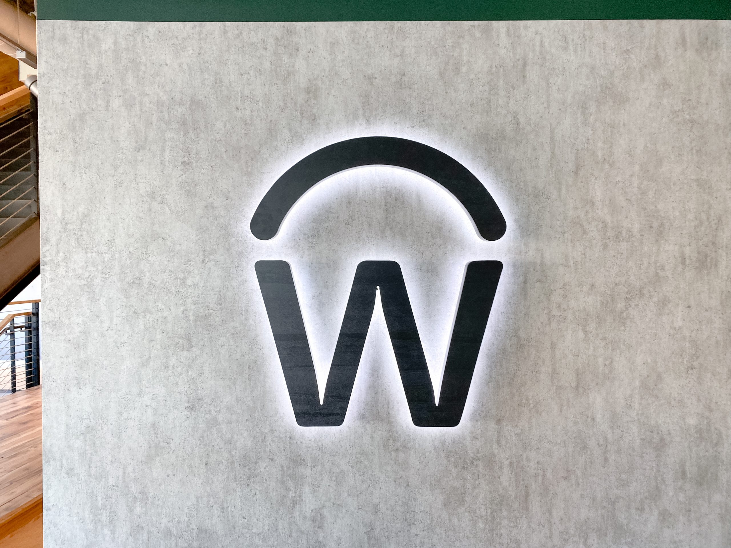 Illuminated, backlit, aged metal sign on concrete lobby wall for the San Francisco office of Workday, a software company.