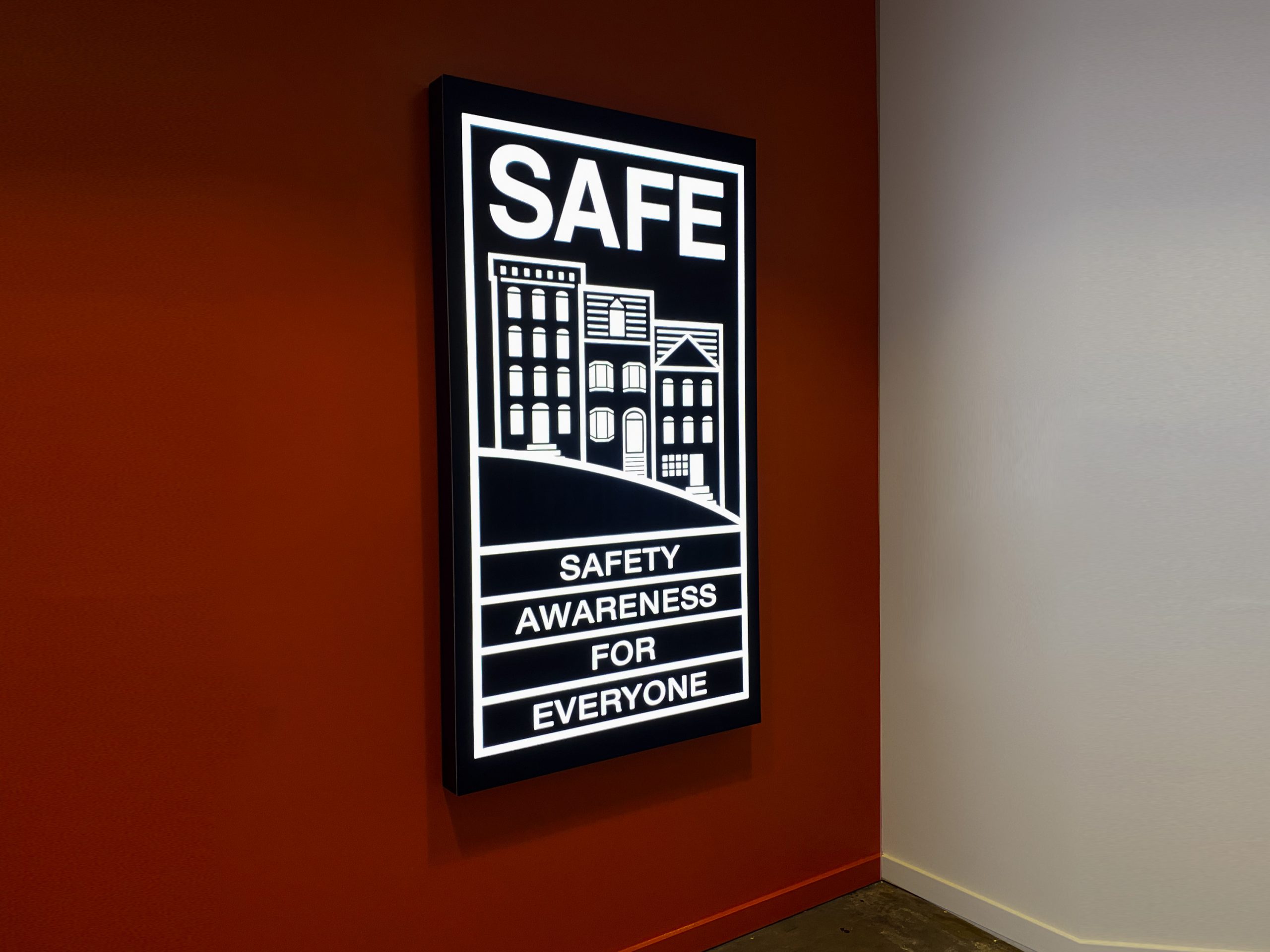 Illuminated, black-and-white, poster-style lightbox sign for the elevator vestibule of SAFE, an organization that partners with the San Francisco Police Department to educate and empower San Franciscans to build safer neighborhoods.