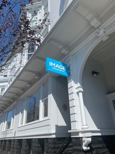 Cyan blue, rigid, boxed blade sign with raised dimensional white letters/logo for Image Orthodontics, an orthodontic office in San Francisco, CA.