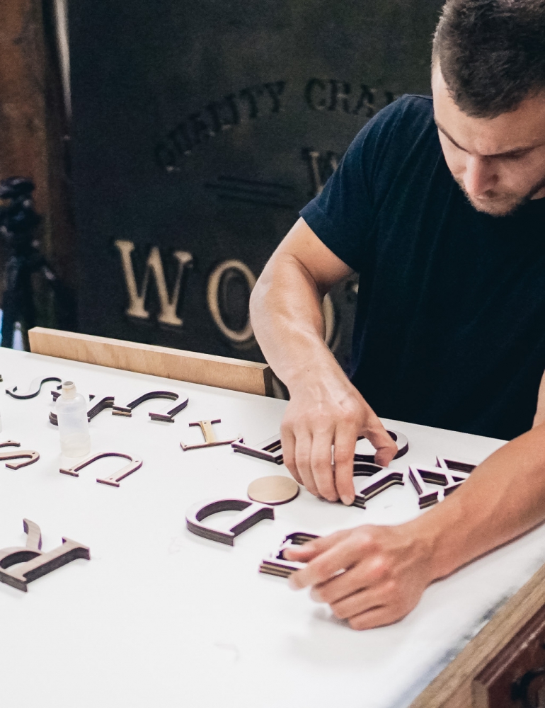 Lush hanging retail blade sign in black stained wood with raised dimensional white letters - process