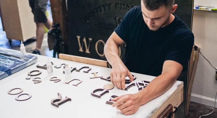 Lush hanging retail blade sign in black stained wood with raised dimensional white letters - process