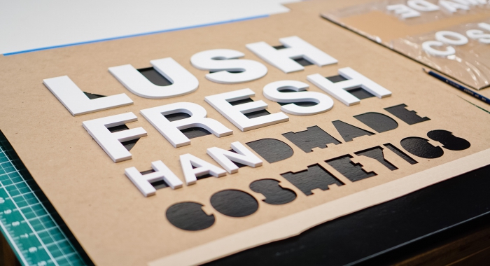 Lush hanging retail blade sign in black stained wood with raised dimensional white letters - process
