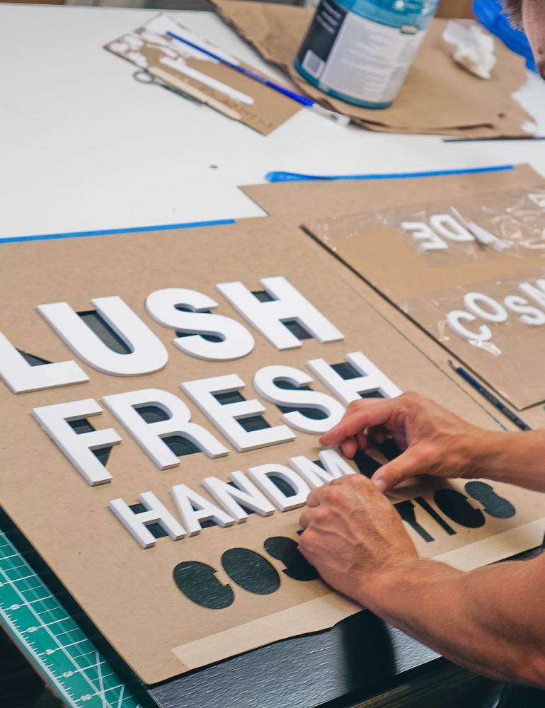 Lush hanging retail blade sign in black stained wood with raised dimensional white letters - process