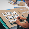 Lush hanging retail blade sign in black stained wood with raised dimensional white letters - process