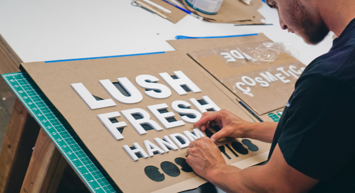 Lush hanging retail blade sign in black stained wood with raised dimensional white letters - process