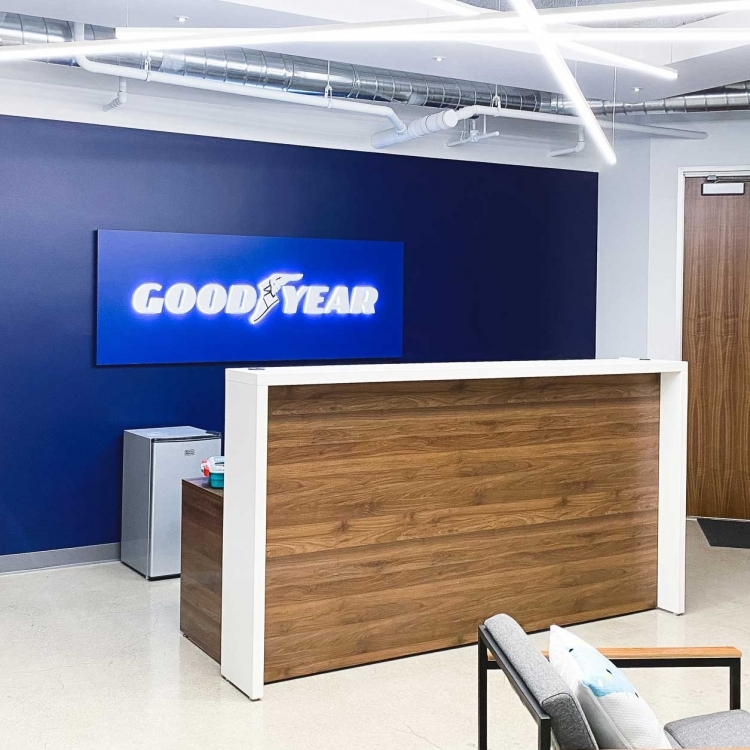 Illuminated, blue, edge-lit lobby sign behind reception desk for the San Francisco office of Goodyear, a tire manufacturer.