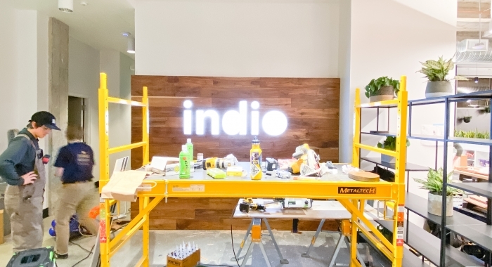 Full wall installation with dark wood and an illuminated, built-in logo for the San Francisco lobby of Indio, a company that simplifies the insurance application process for brokers and their clients.