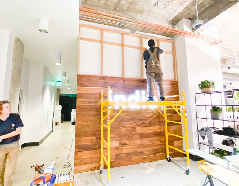 Full wall installation with dark wood and an illuminated, built-in logo for the San Francisco lobby of Indio, a company that simplifies the insurance application process for brokers and their clients.