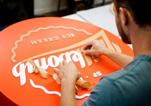 Red circular blade sign with white script for Milkbomb, a sweet stop for donut ice cream sandwiches.